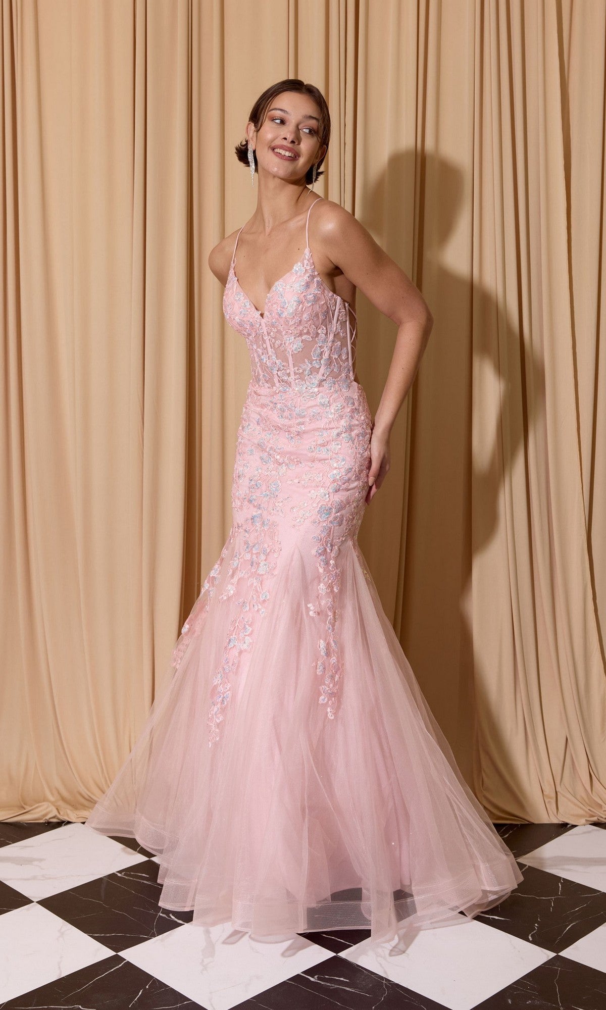 A woman in the Eureka 9696 Sequin-Floral Long Mermaid Prom Dress in pink stands on a black and white tiled floor before beige curtains.